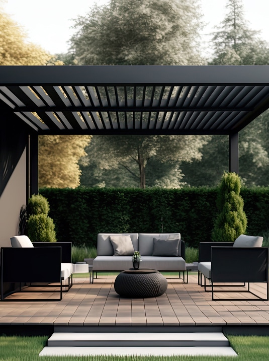 Salon de jardin design sous pergola bioclimatique noire. Canapé, fauteuils et table basse sur un deck en bois entouré de verdure.
