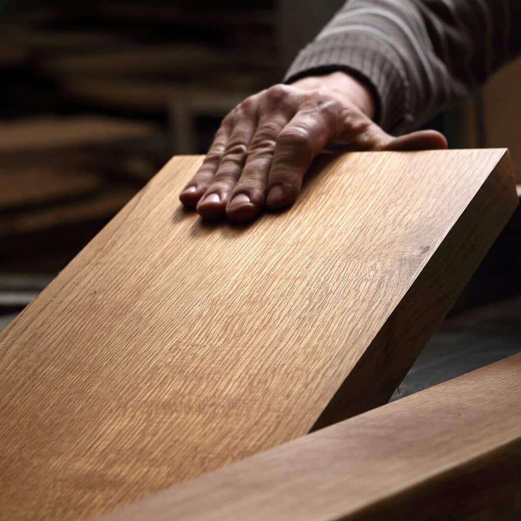 Artisanat du bois : Touchez la qualité du bois massif. Main d'artisan touchant doucement la surface d'une planche de bois clair, vérifiant la texture et la qualité du bois.