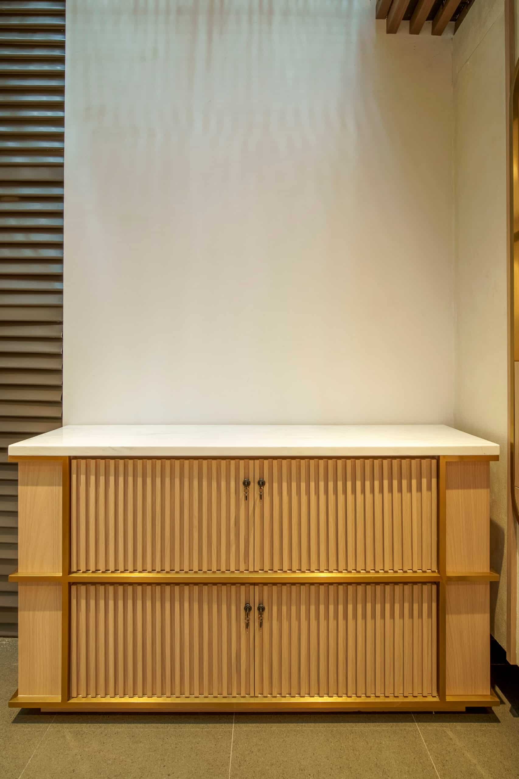 Buffet en bois clair avec crédence marbrée, portes à lattes verticales et cadres dorés. Meuble de rangement moderne.