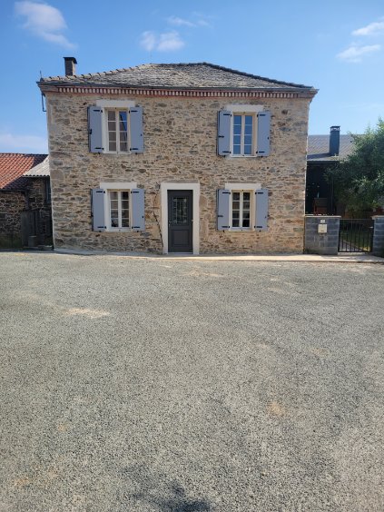 Maison traditionnelle en pierre avec volets bleu ciel et porte foncée devant une grande cour en gravier.